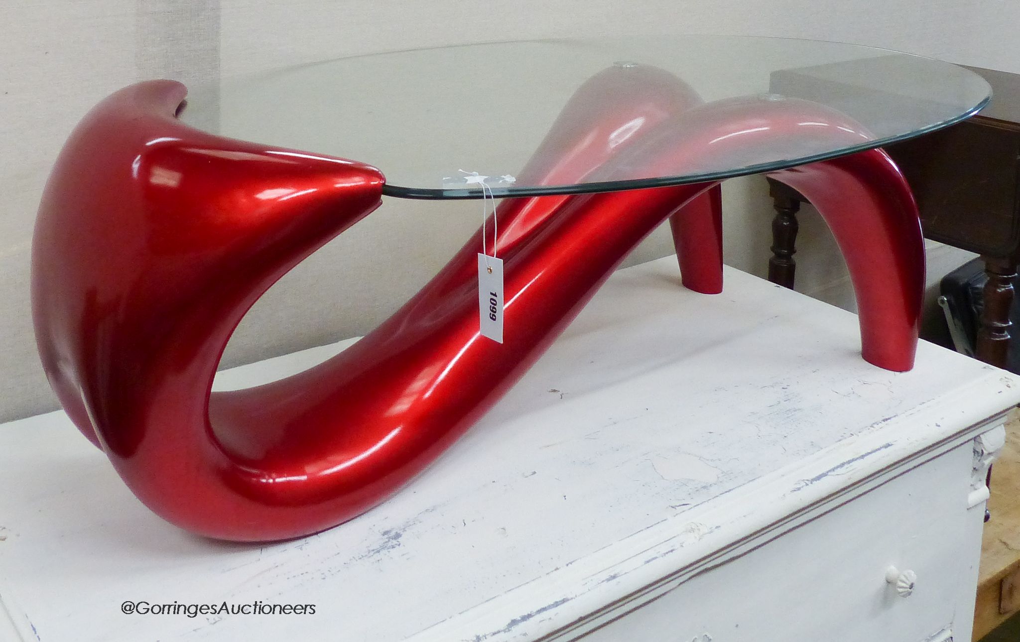 A contemporary red composition body form oval glass top table. W-124cm, D-70cm, H-41cm.